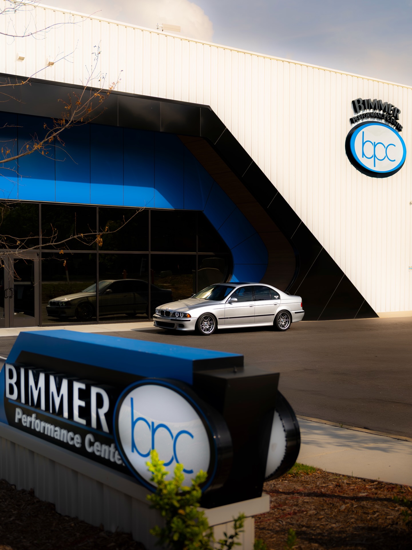 Silver E39 BMW M5 parked outside Bimmer Performance Center beside the shop signage