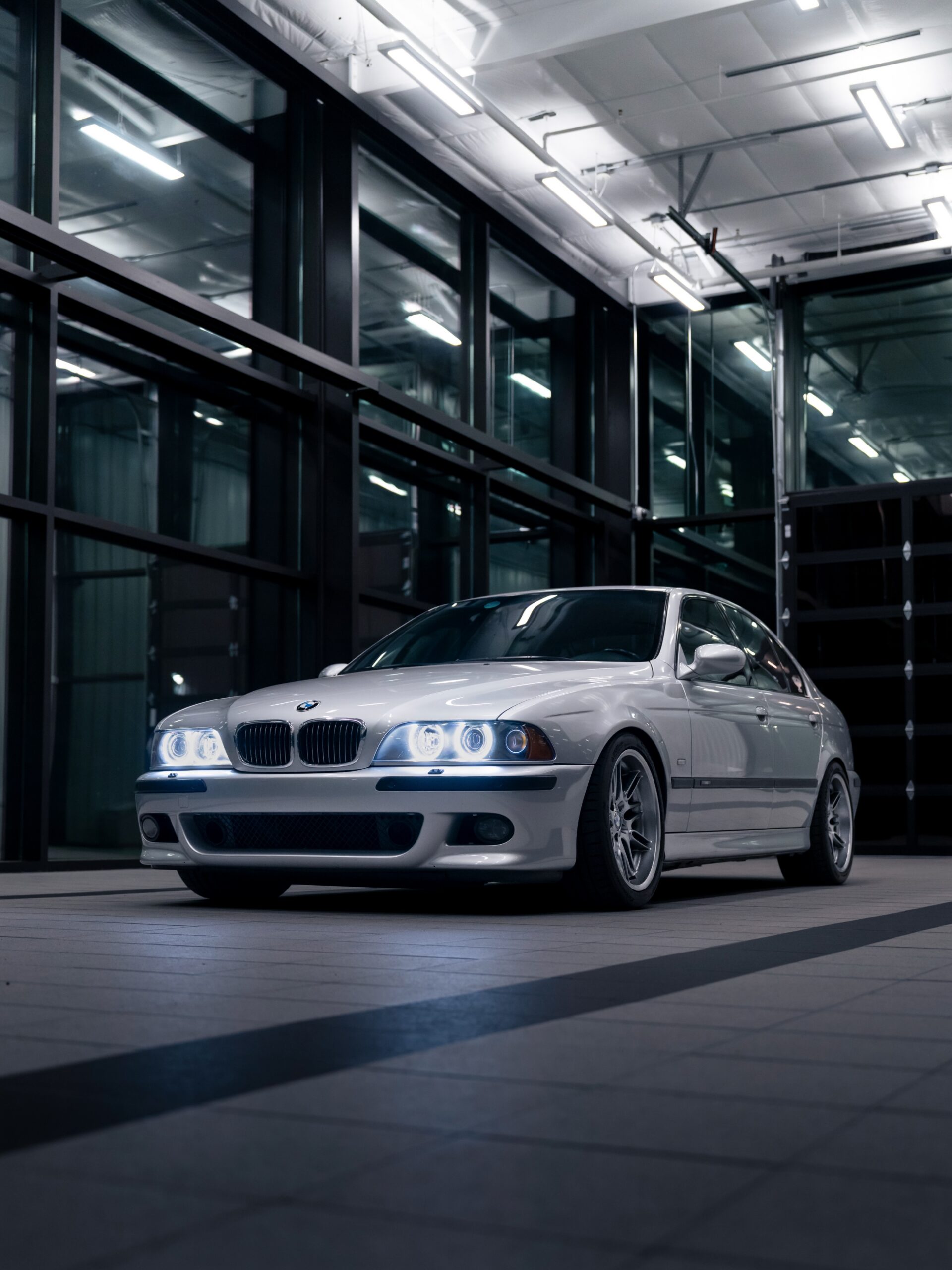 Front three-quarter view of the silver E39 BMW M5 with its headlights on inside the shop